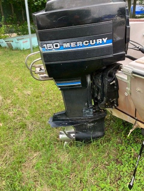 A mercury outboard motor is sitting in the grass next to a boat.