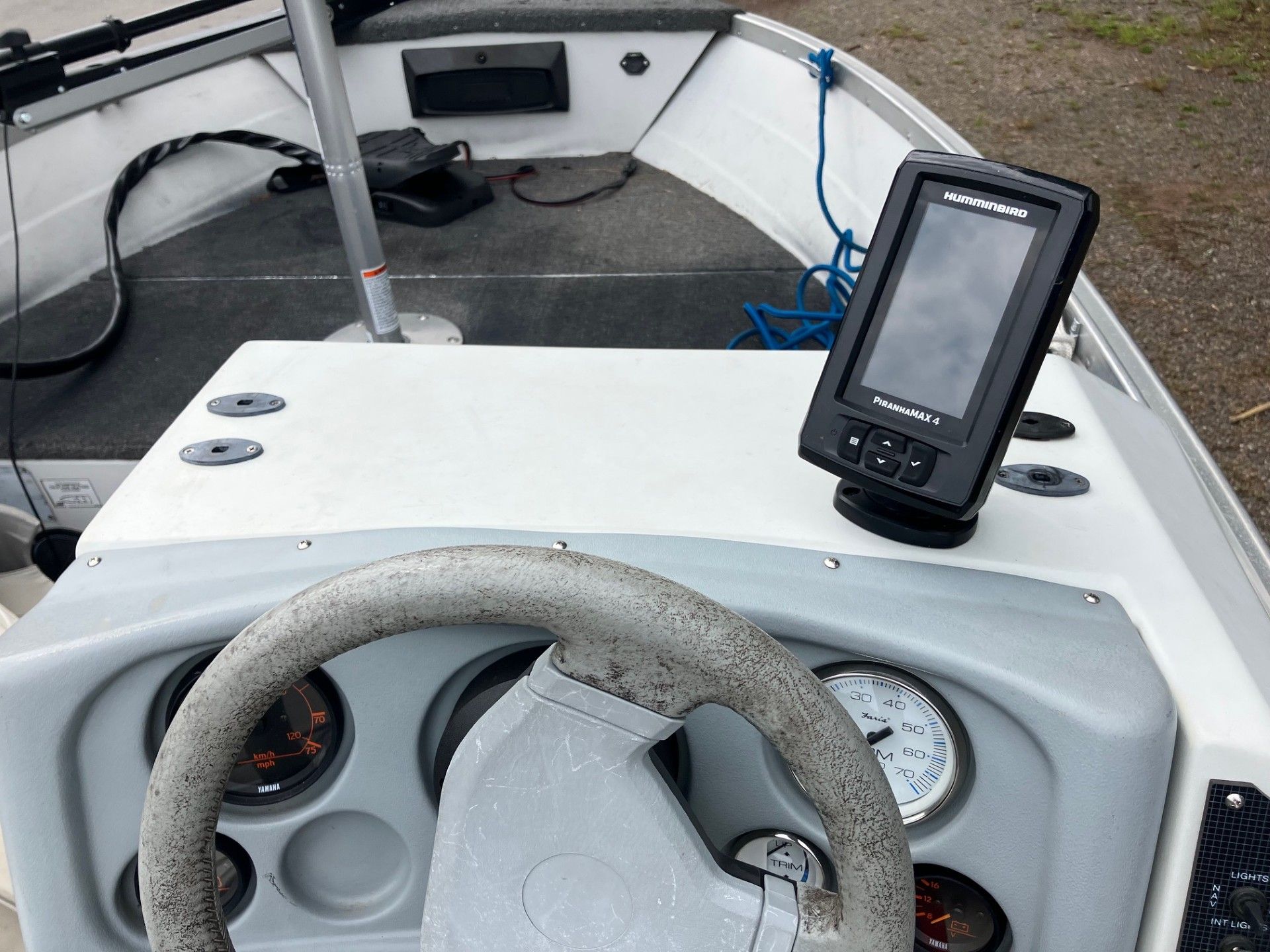 A boat dashboard with a steering wheel, gauges, and a mounted fish finder. The dashboard is white and gray.