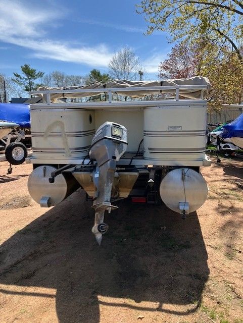 A pontoon boat with a motor is parked in a dirt lot.