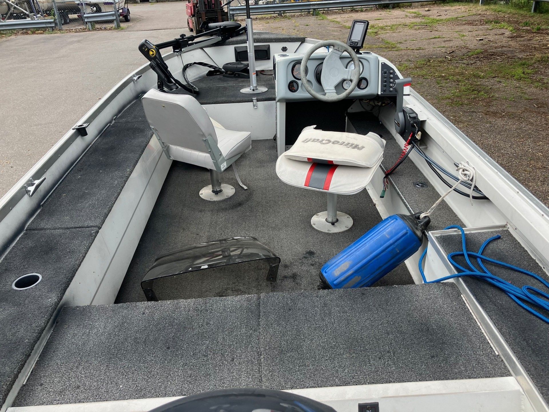 Interior of a fishing boat: gray carpet, white seats, blue fender, steering wheel, and electronic displays.