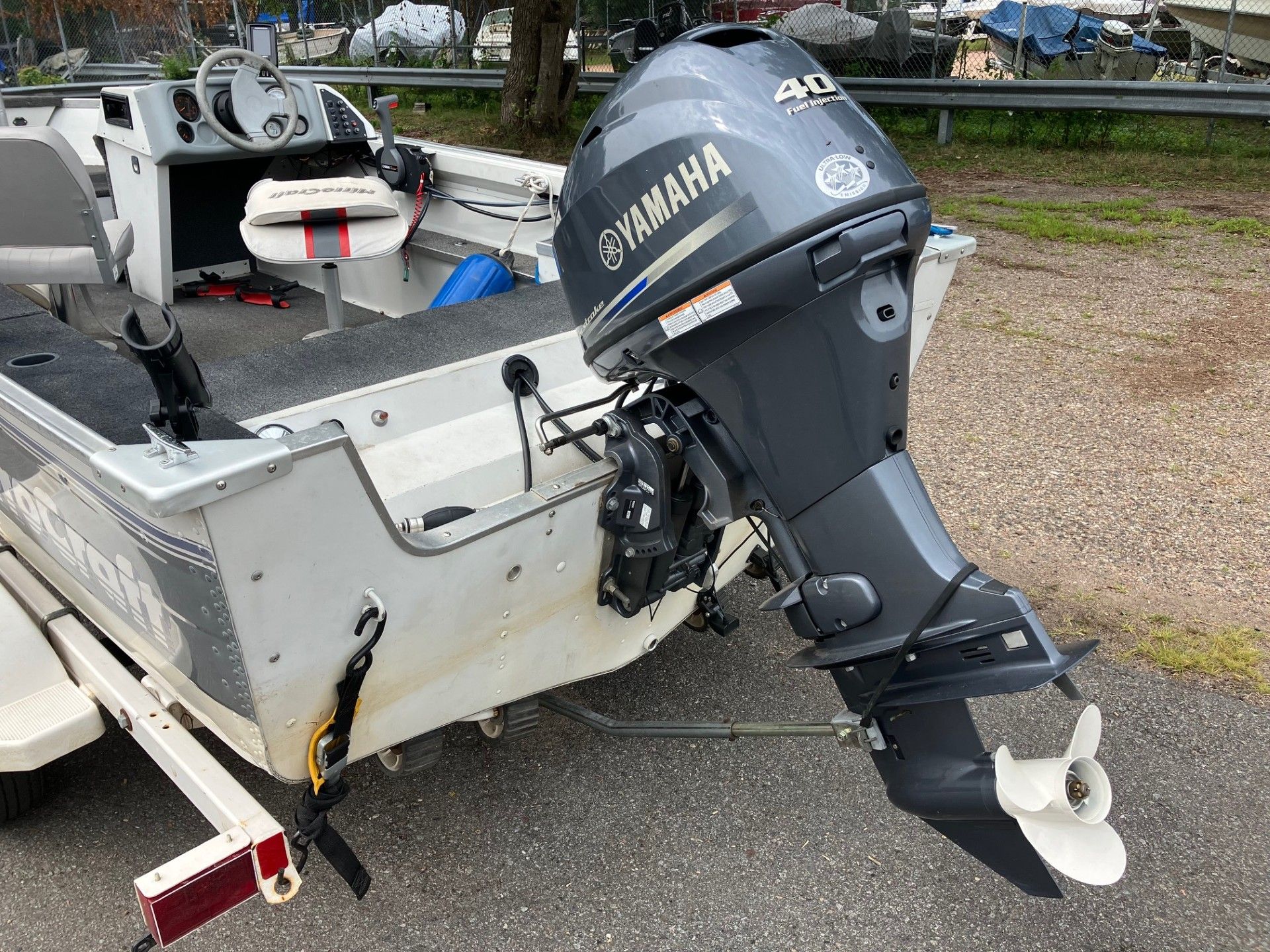 Silver boat with a Yamaha 40 outboard motor parked on a paved area. The boat has a gray interior and is attached to a trailer.