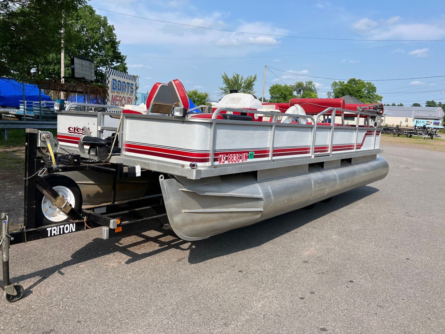 Pontoon boat with red accents on a trailer. It sits outside on a sunny day.