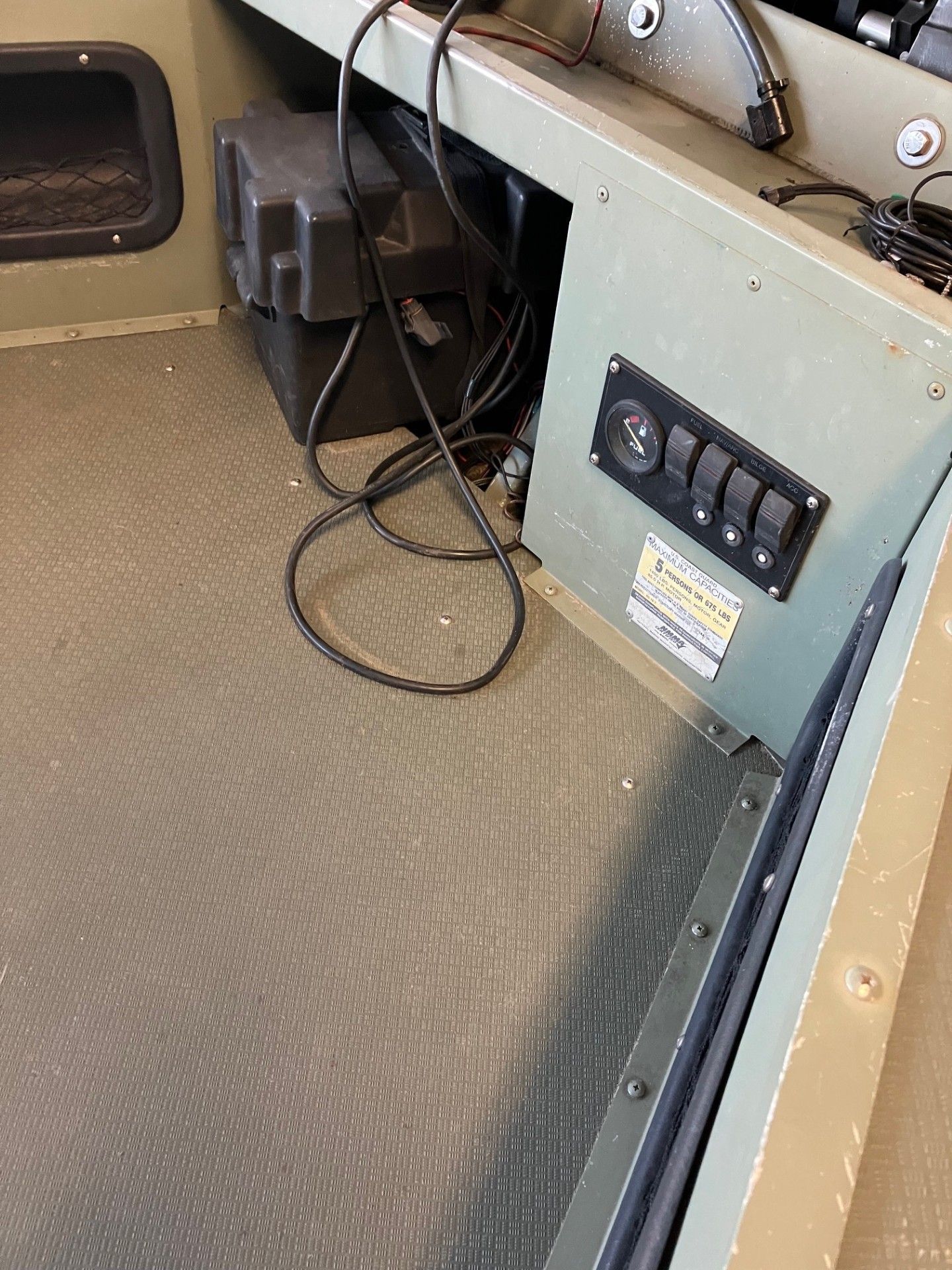 Boat interior with black battery, switches, and wiring on a green panel.
