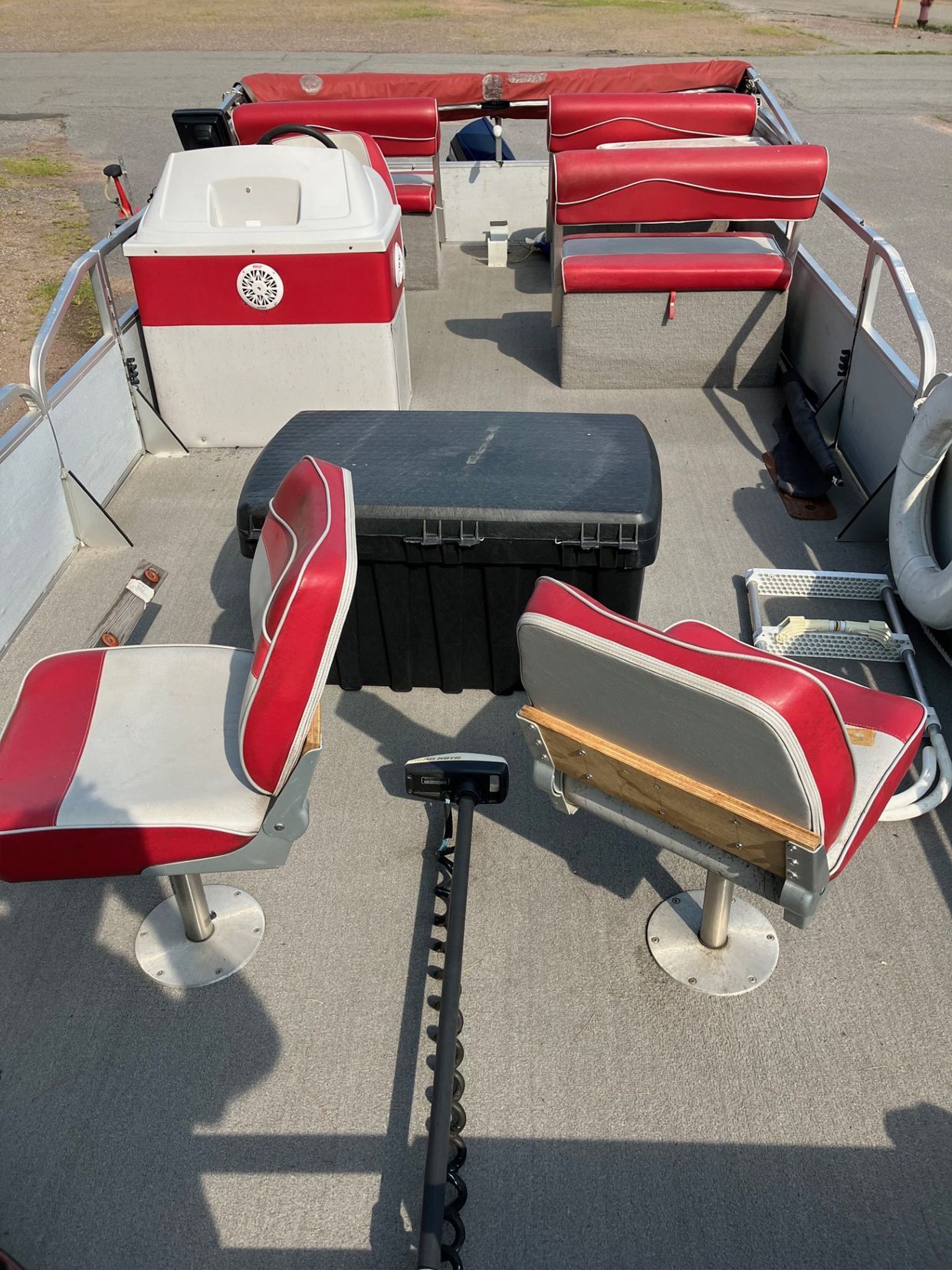 Interior of a red and white fishing boat on a concrete surface. Two seats face each other in the foreground, with storage and seating in the background.