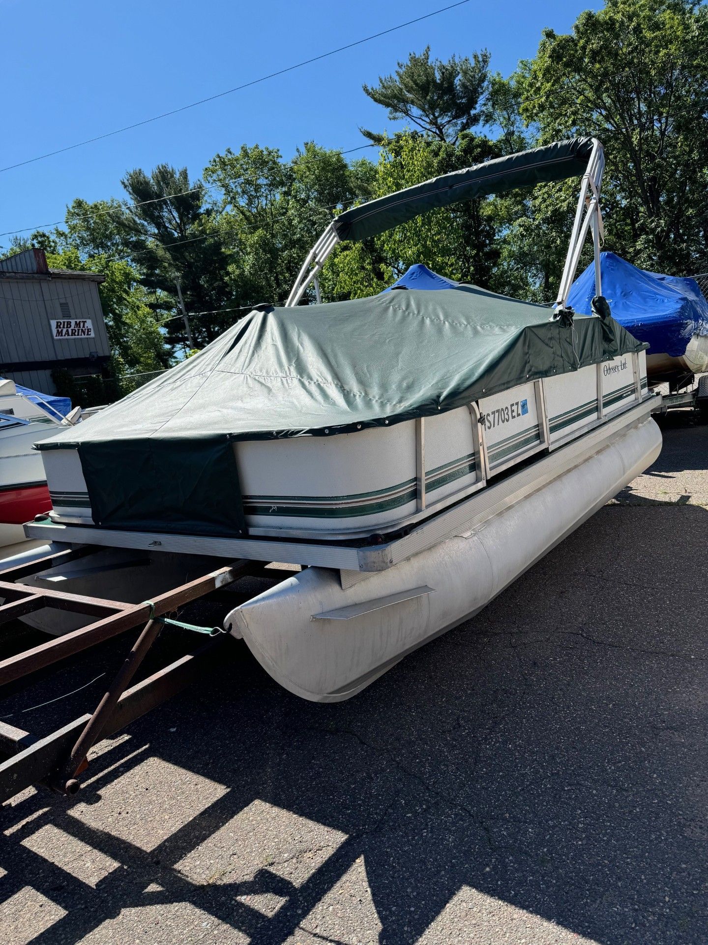 A pontoon boat with a green cover is parked on the side of the road