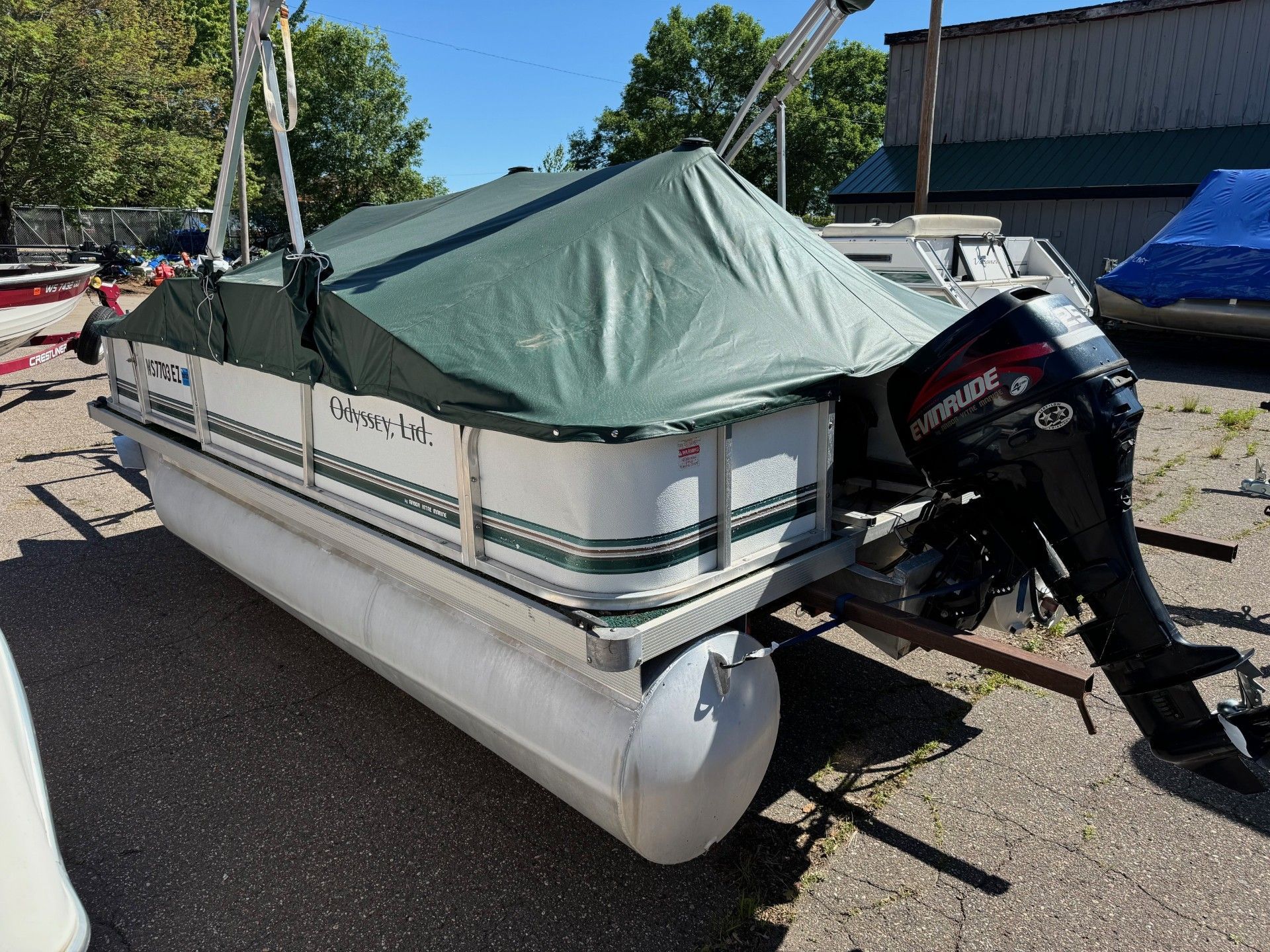 A pontoon boat with a green cover on it is parked in a parking lot