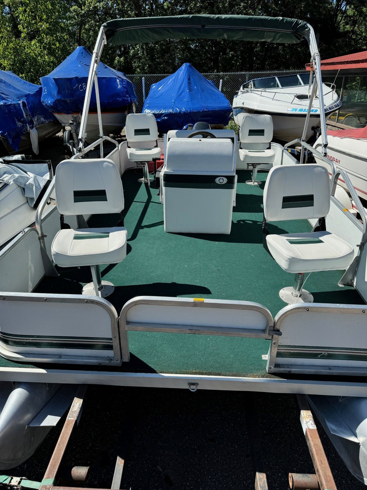 A pontoon boat is parked in a lot with other boats