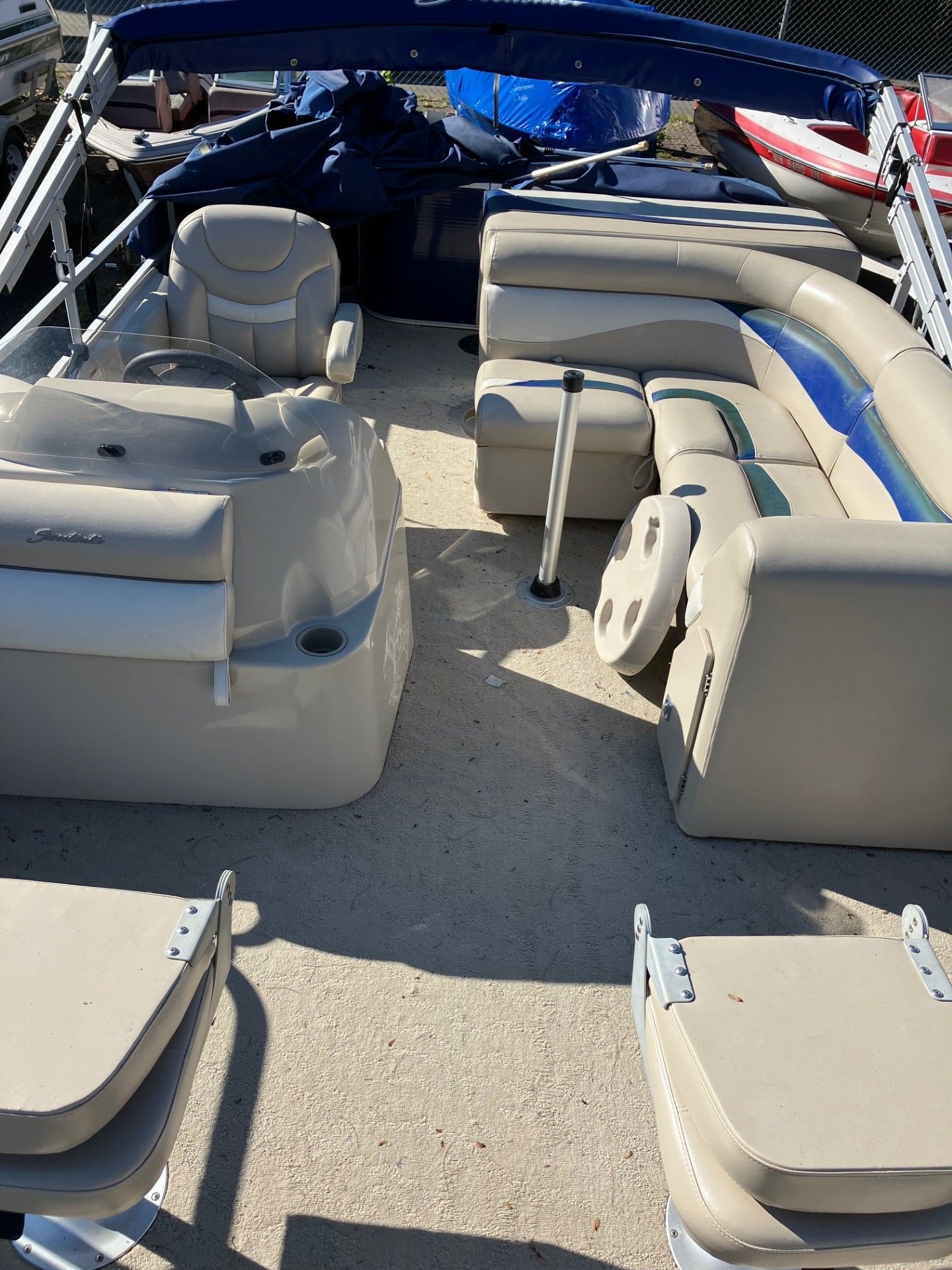Pontoon boat interior with beige seats, blue accents, and a dark blue canopy.