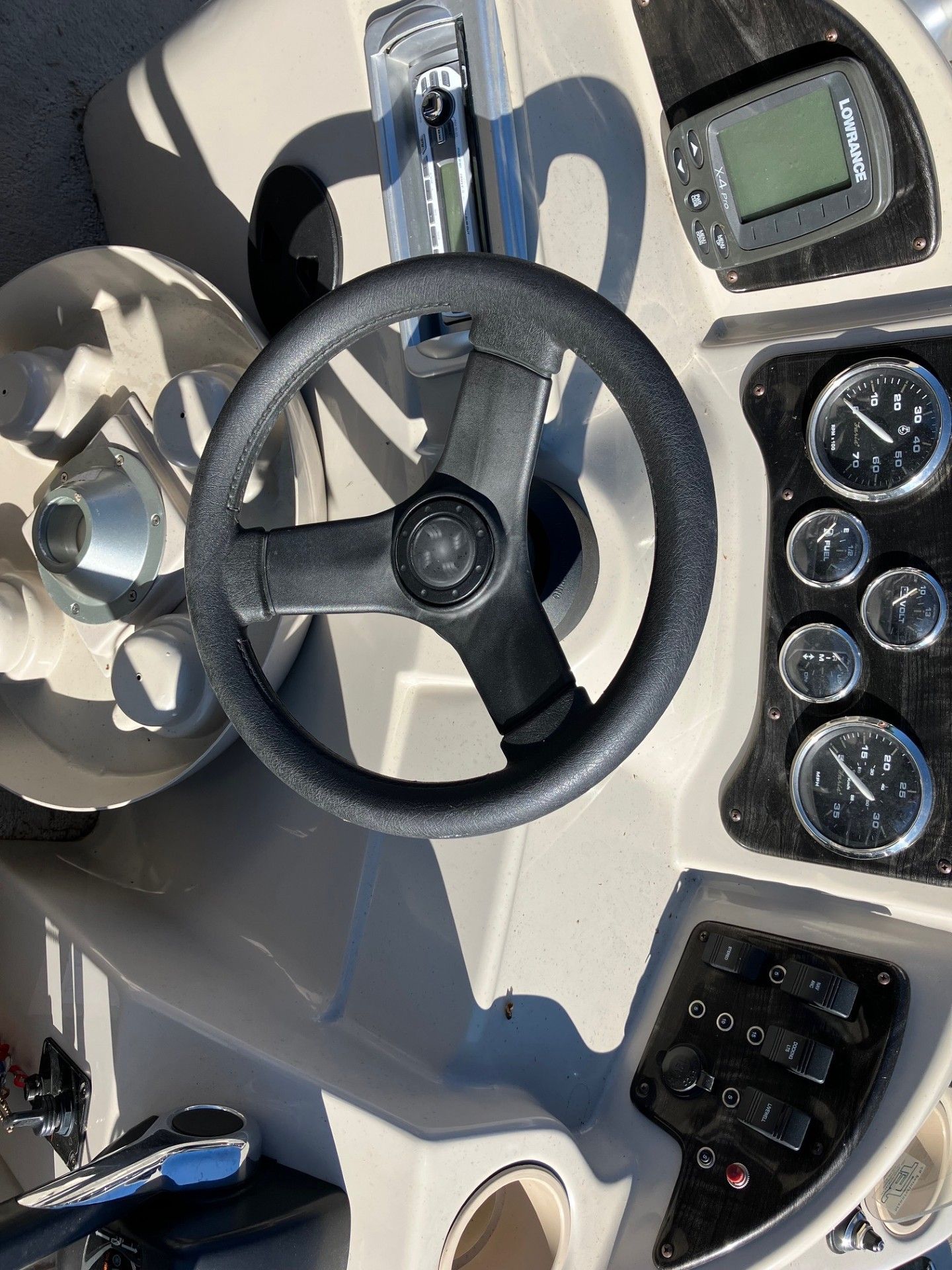 Boat's dashboard with black steering wheel, gauges, and control panel. Sunlight reflecting.