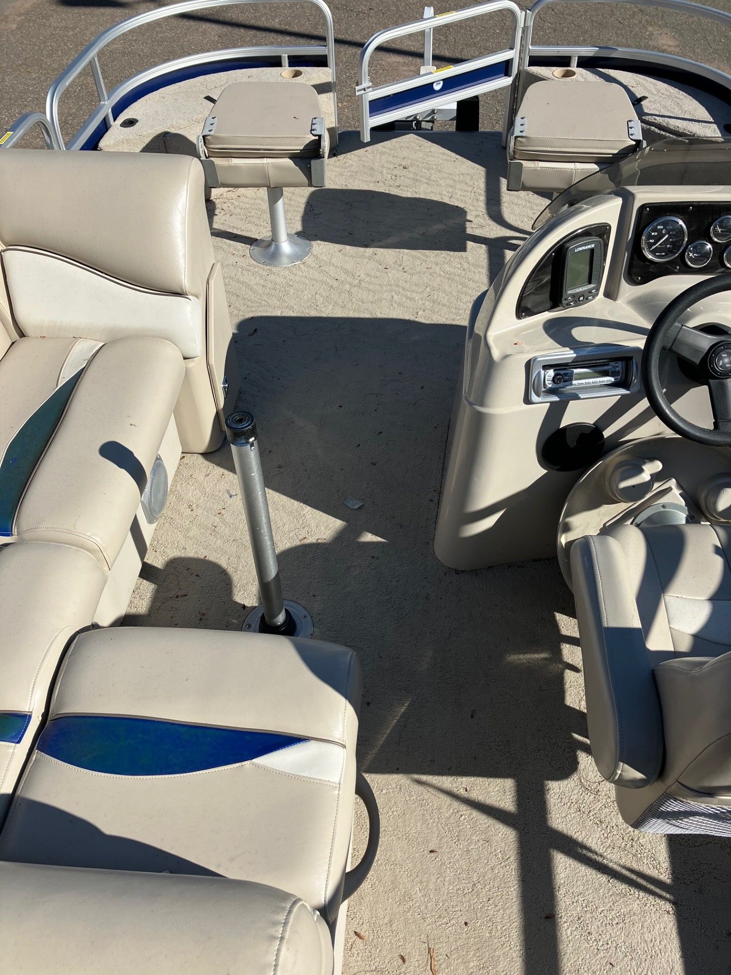 Interior of a pontoon boat with beige seating, steering wheel, and gauges.