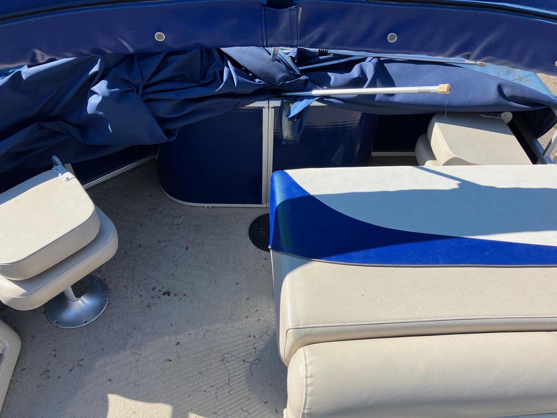 Inside of a blue and beige pontoon boat. Shows seating, tarp, and a pole.