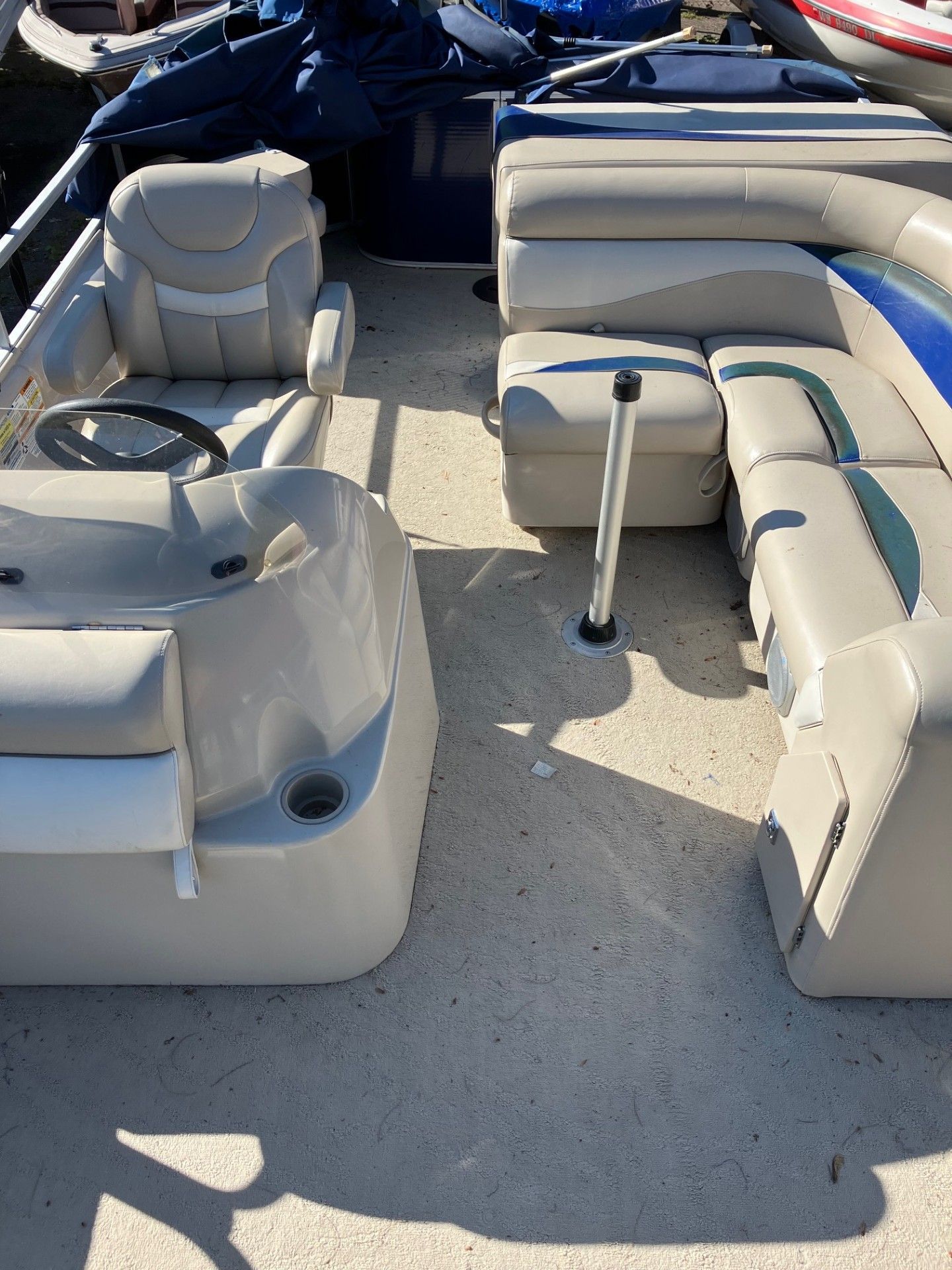 Interior of a pontoon boat with beige and blue seating, a steering wheel, and a metal support pole.
