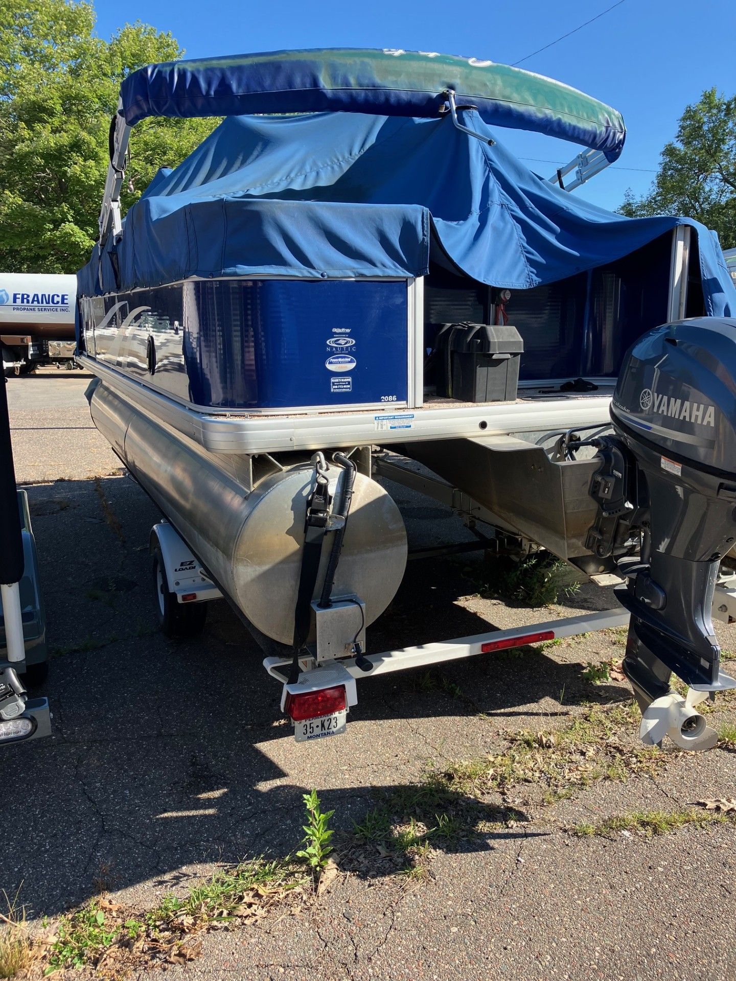 Pontoon boat on trailer, blue cover, blue storage box, and a Yamaha outboard motor.