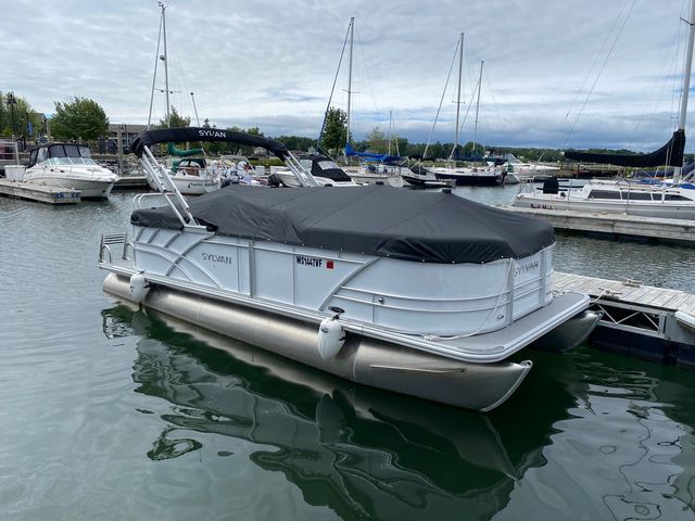 A pontoon boat with a black cover is docked at a marina