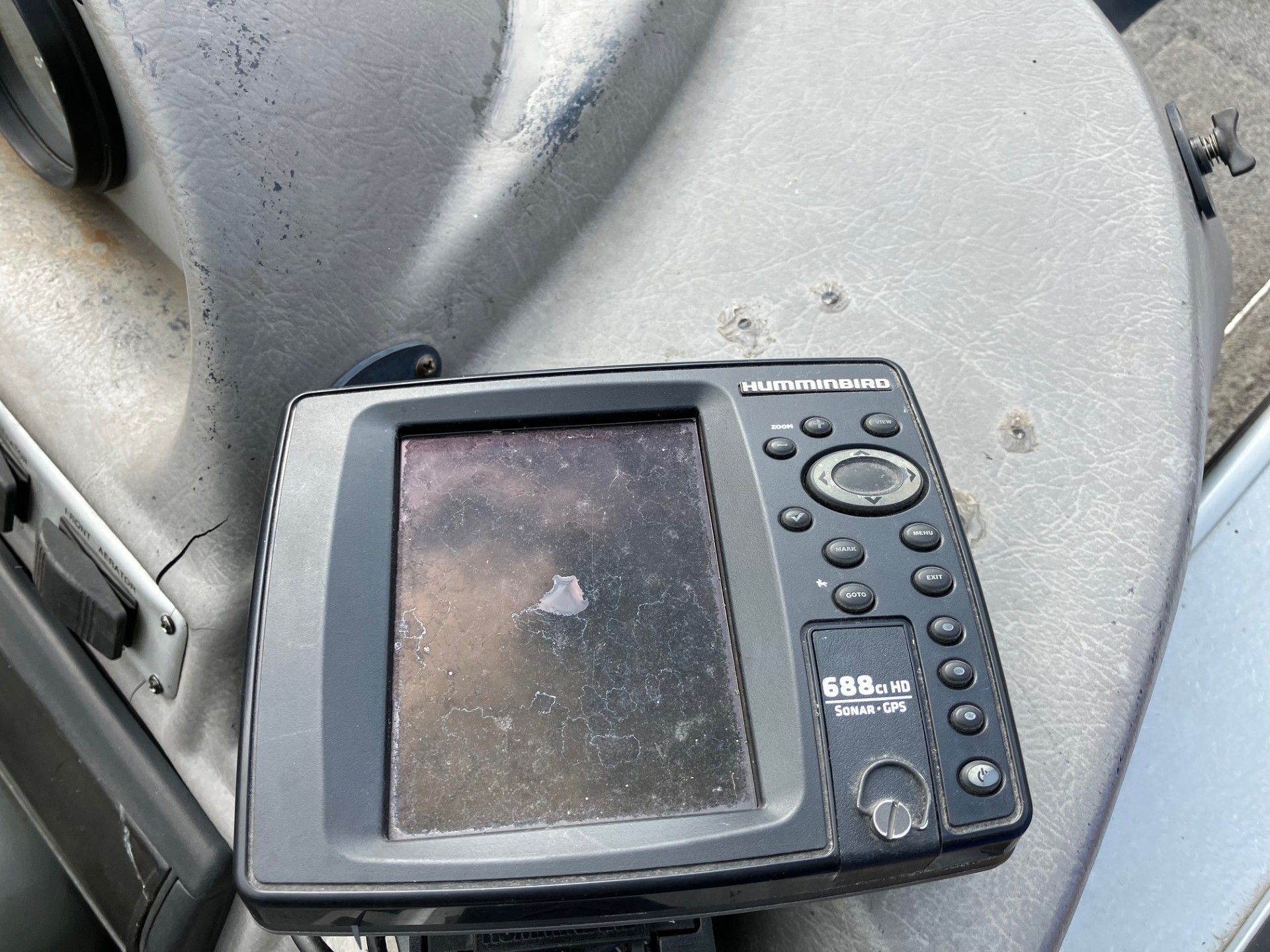 Fishing boat's gray dashboard with a fish finder. The fish finder is black with several buttons and a screen.