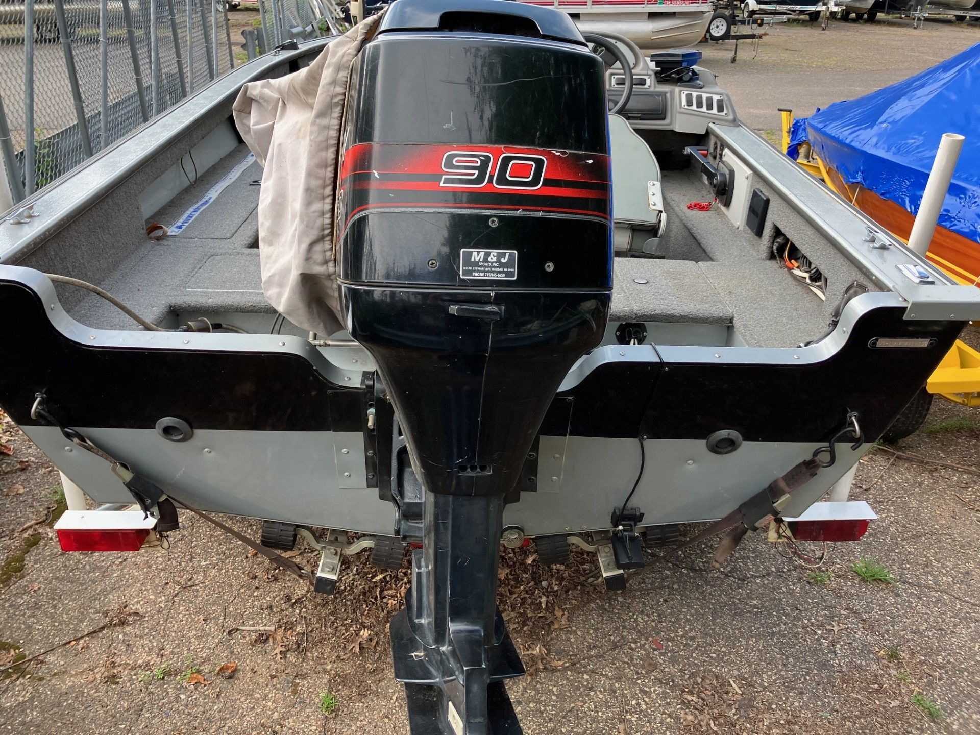 A gray aluminum fishing boat with a black 90 HP motor, backed on a gravel lot.
