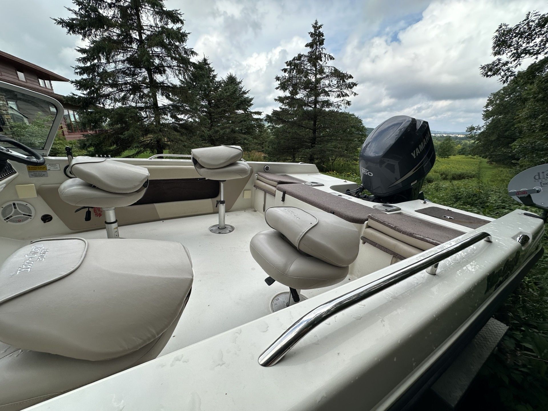 A white boat with a mercury outboard motor is parked in the woods.