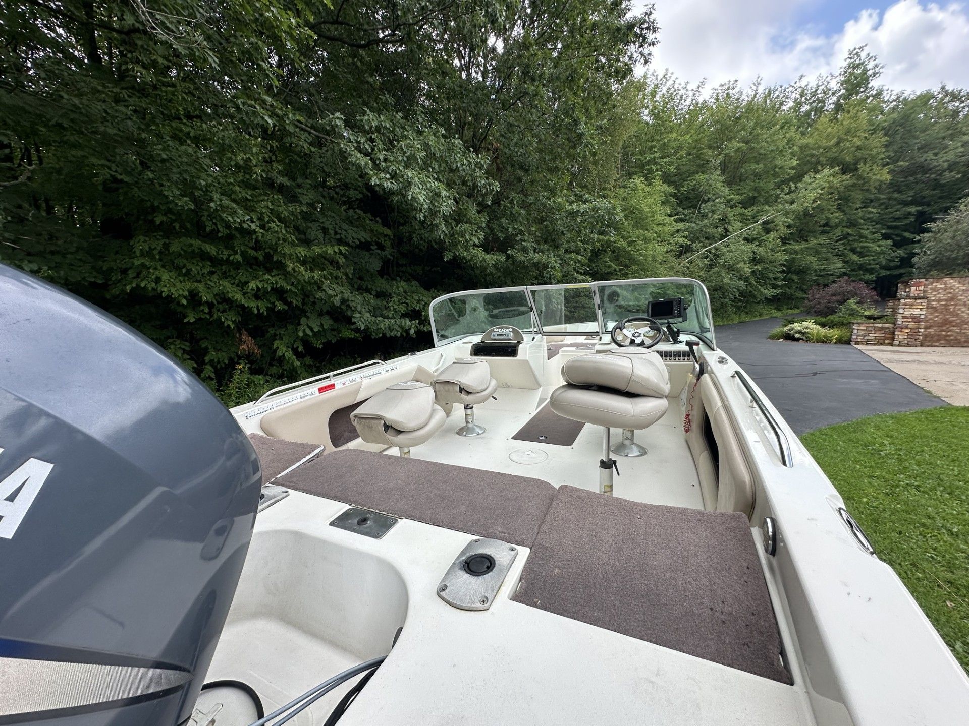 A white boat with a yamaha engine is parked in a driveway.