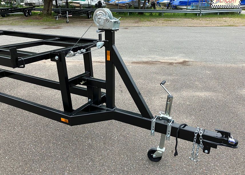 Black trailer frame with two axles, each with two tires on a light gray surface.