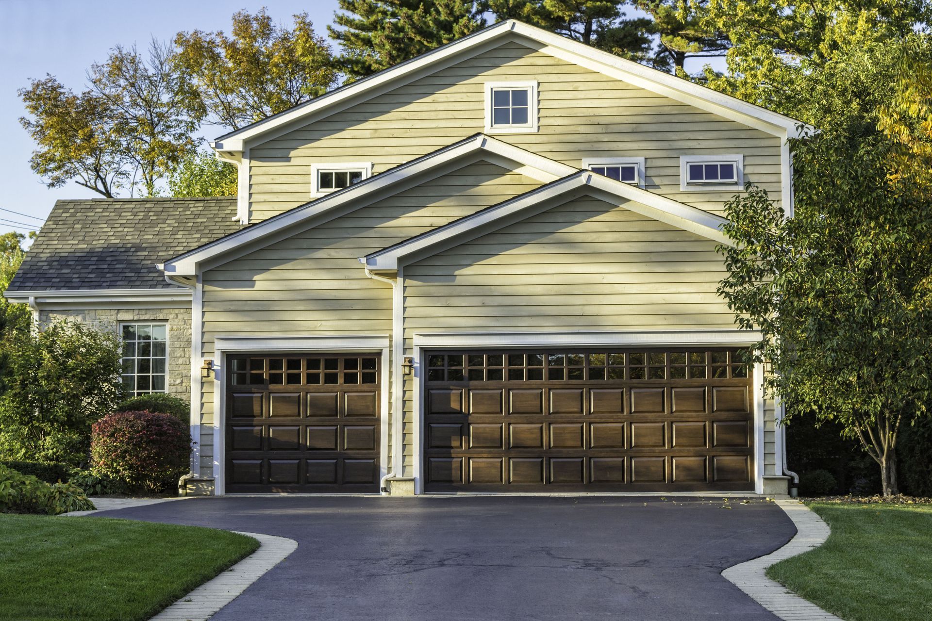 Two-story house with brown garage doors, asphalt driveway, and green lawn.