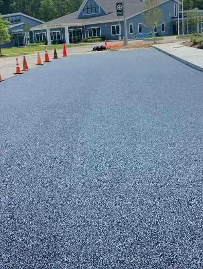 Freshly paved asphalt with orange safety cones; building in background.