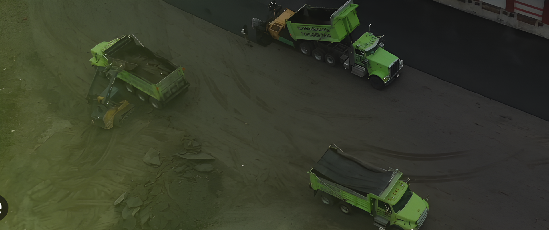 Overhead shot of construction site; green dump trucks on asphalt.