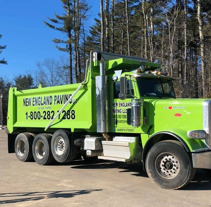 Bright green New England Paving dump truck parked outdoors on a sunny day.