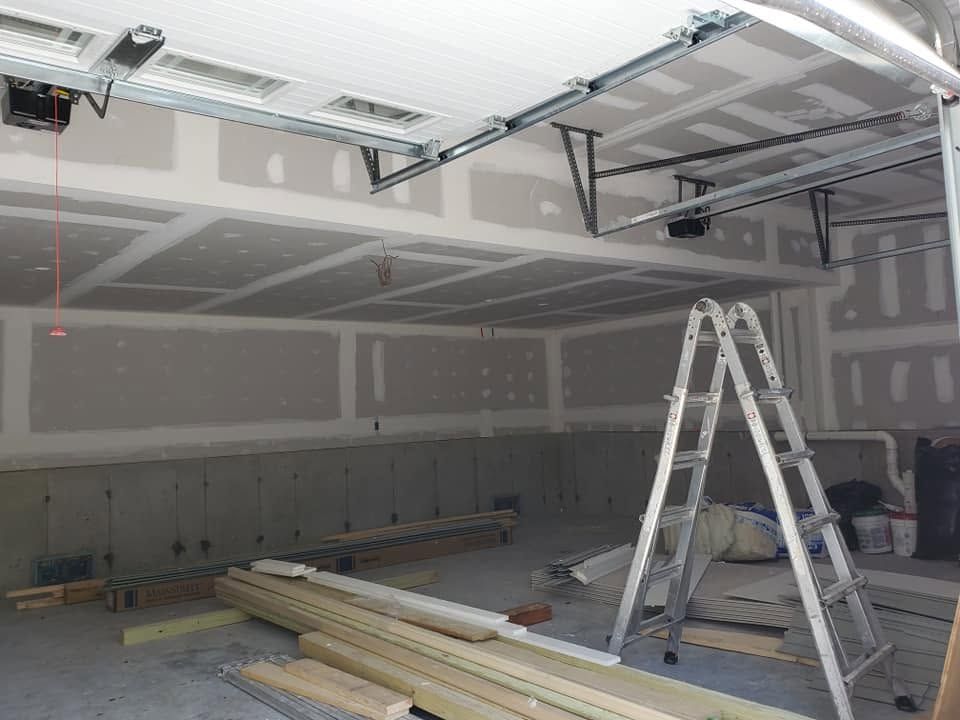Construction site interior with drywall, ladders, and stacked boards in an unfinished room