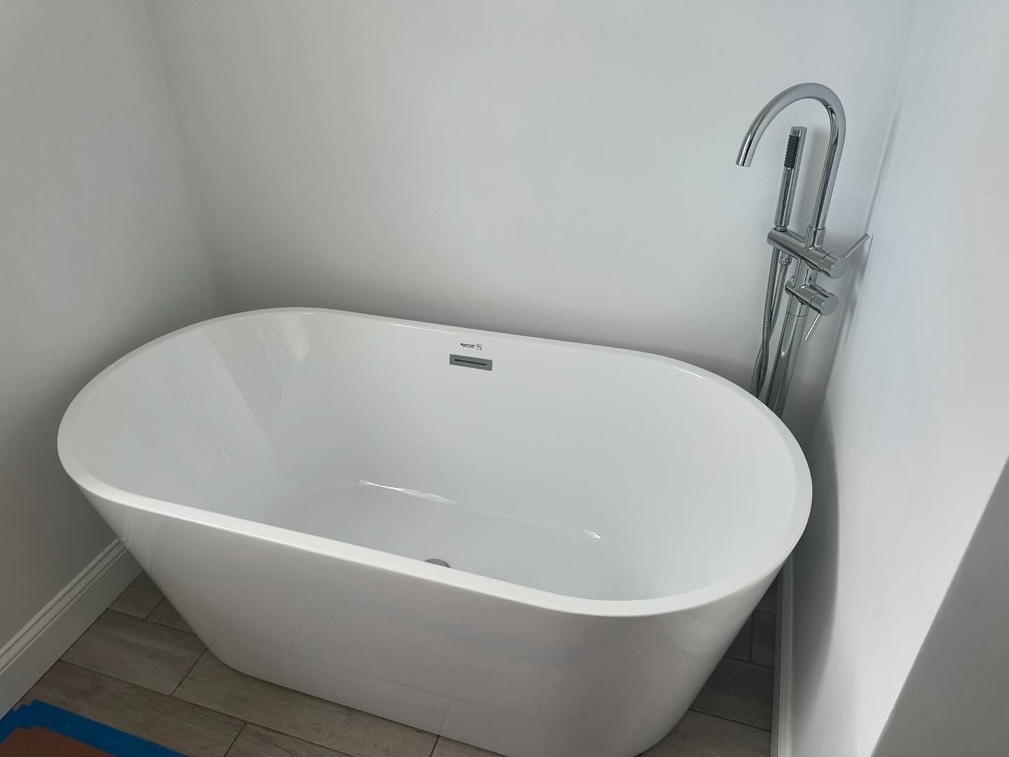 White freestanding bathtub in a minimalist bathroom corner with a chrome faucet