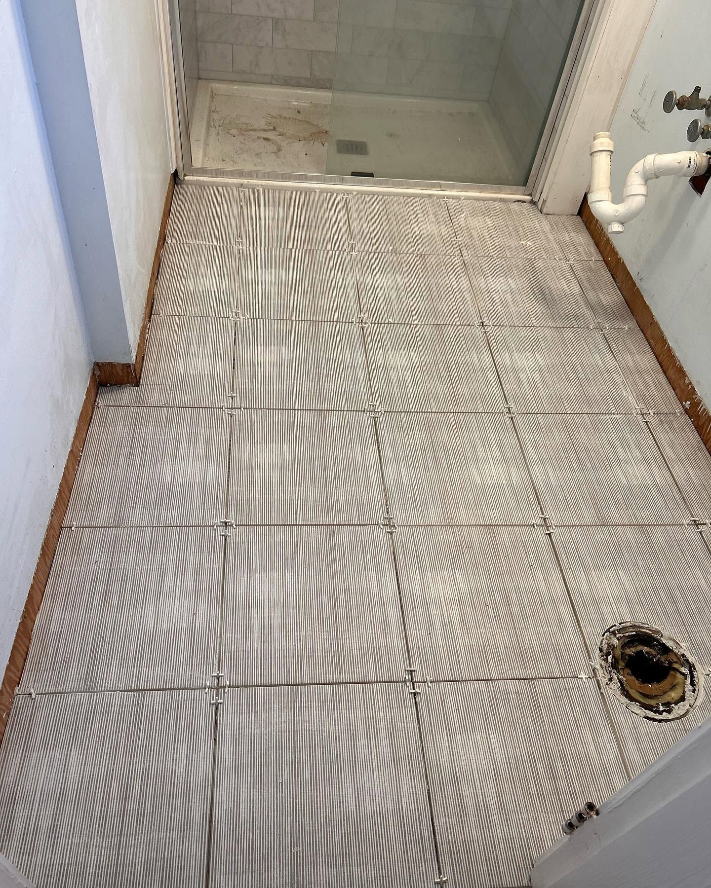 Small tiled shower stall with a drain and white plumbing fixtures.
