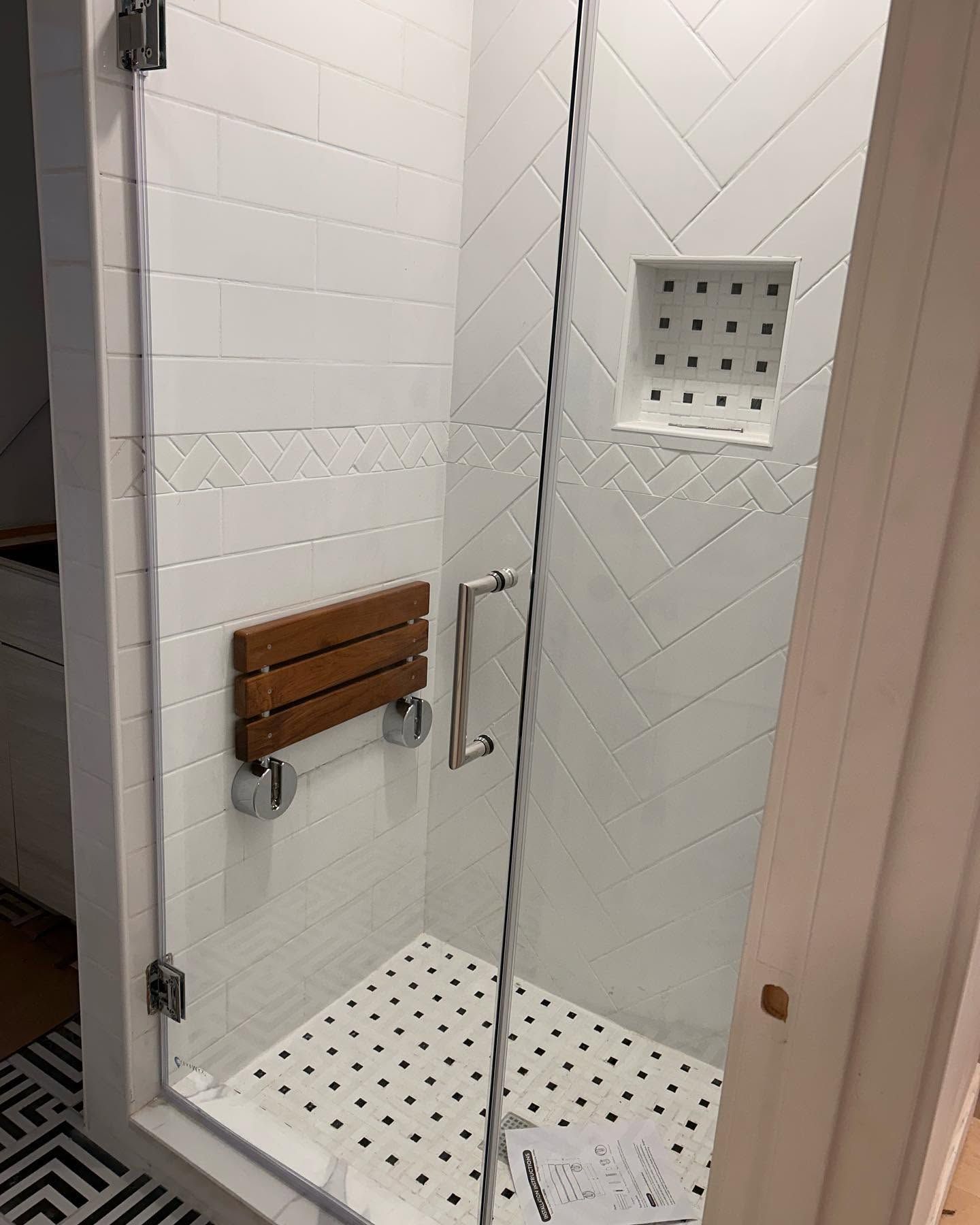 Accessible shower stall with glass door, built-in bench, grab bar, and tiled floor.