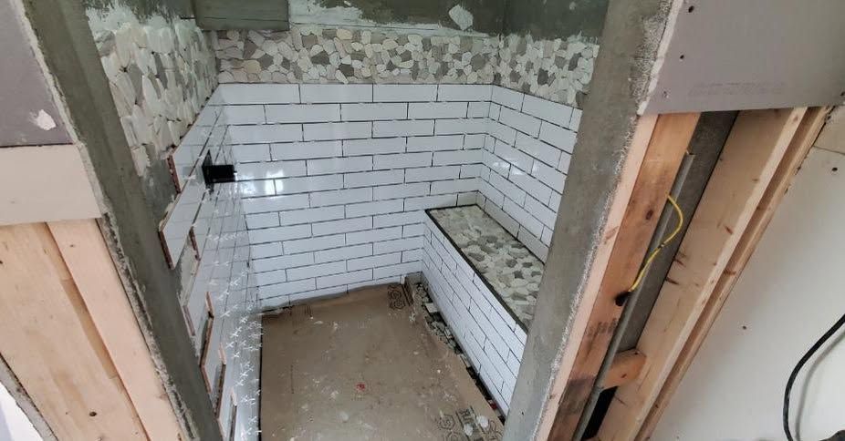 Partially tiled shower stall under renovation, with white subway tiles and exposed framing.