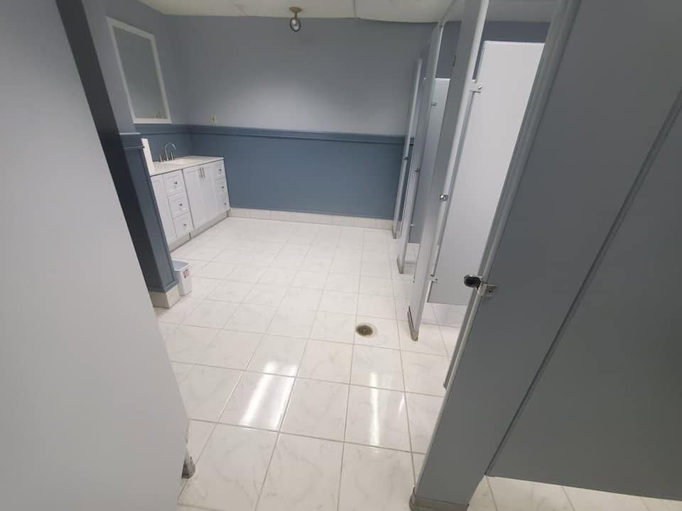 Small tiled laundry room with gray-blue walls, white cabinets, and a door at the right.