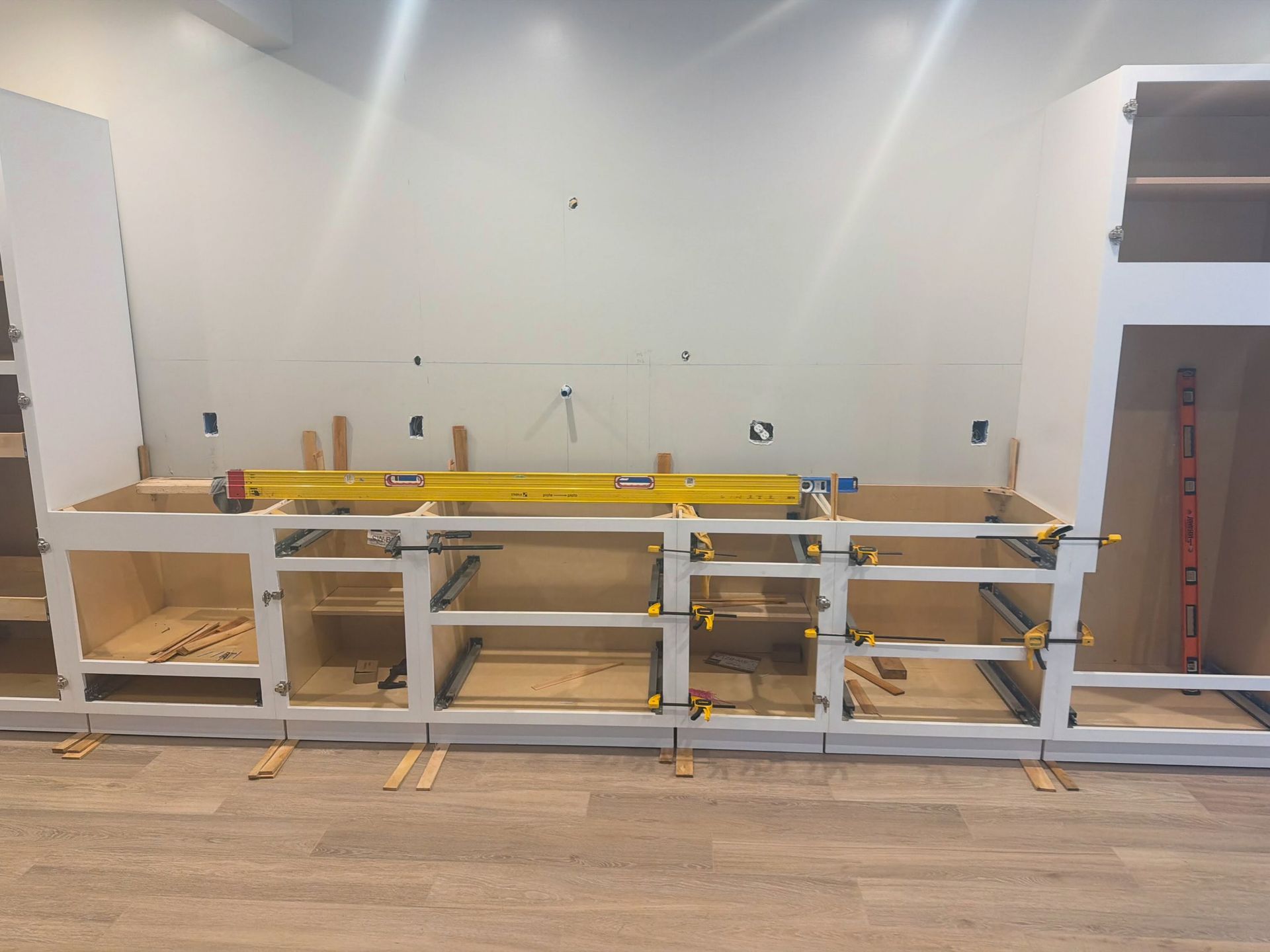 Empty room with unfinished white workbench frame, yellow tools, and cabinets against the wall