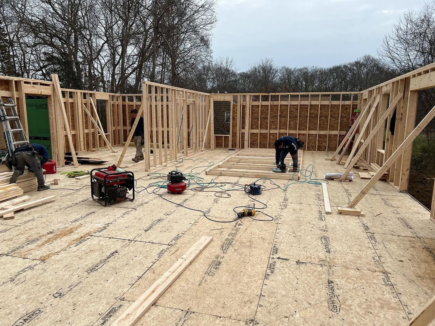 Framed house interior under construction with two workers and tools on a plywood floor