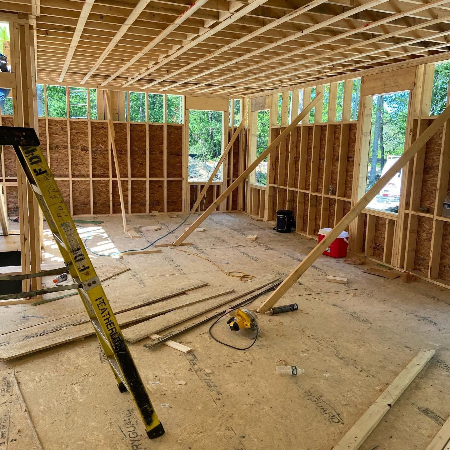 Framed house interior under construction with exposed studs, roof joists, and tools on the floor.