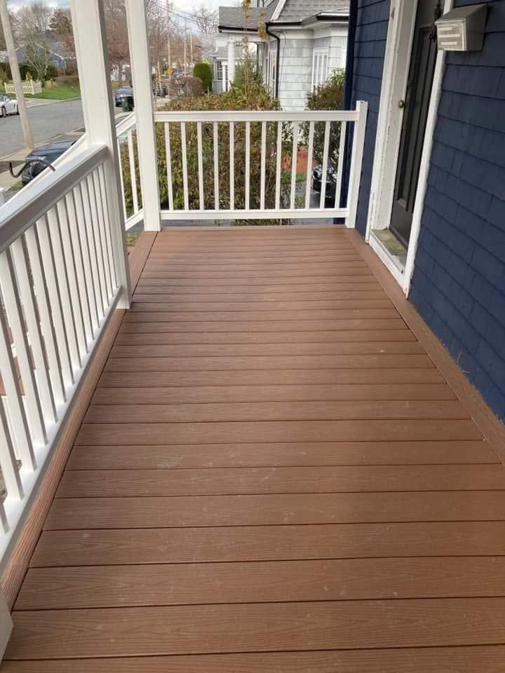Wooden porch deck with white railings and blue house siding overlooking a street and trees.