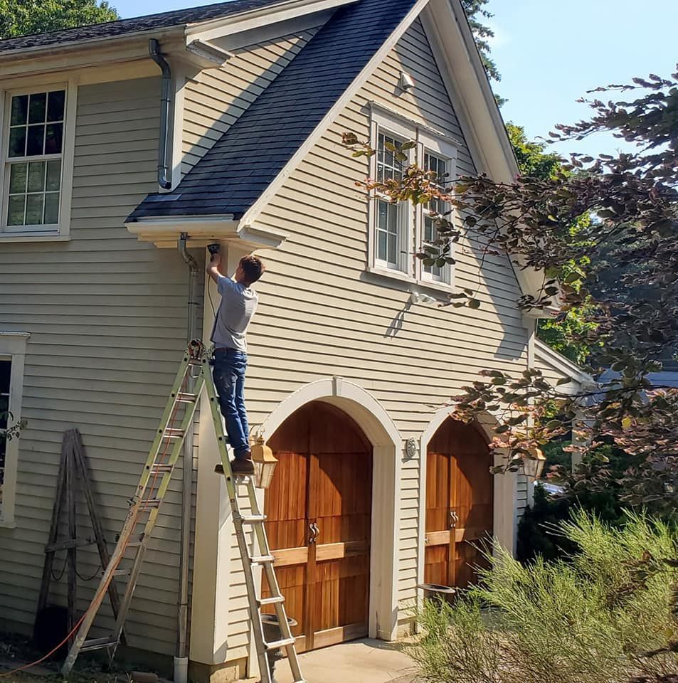 Person on ladder painting the exterior of a beige house with arched wooden garage doors