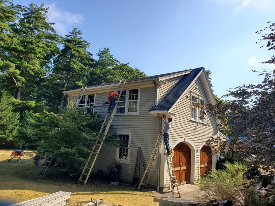 Workers on ladders repairing the roof of a beige house with a detached garage on a sunny day