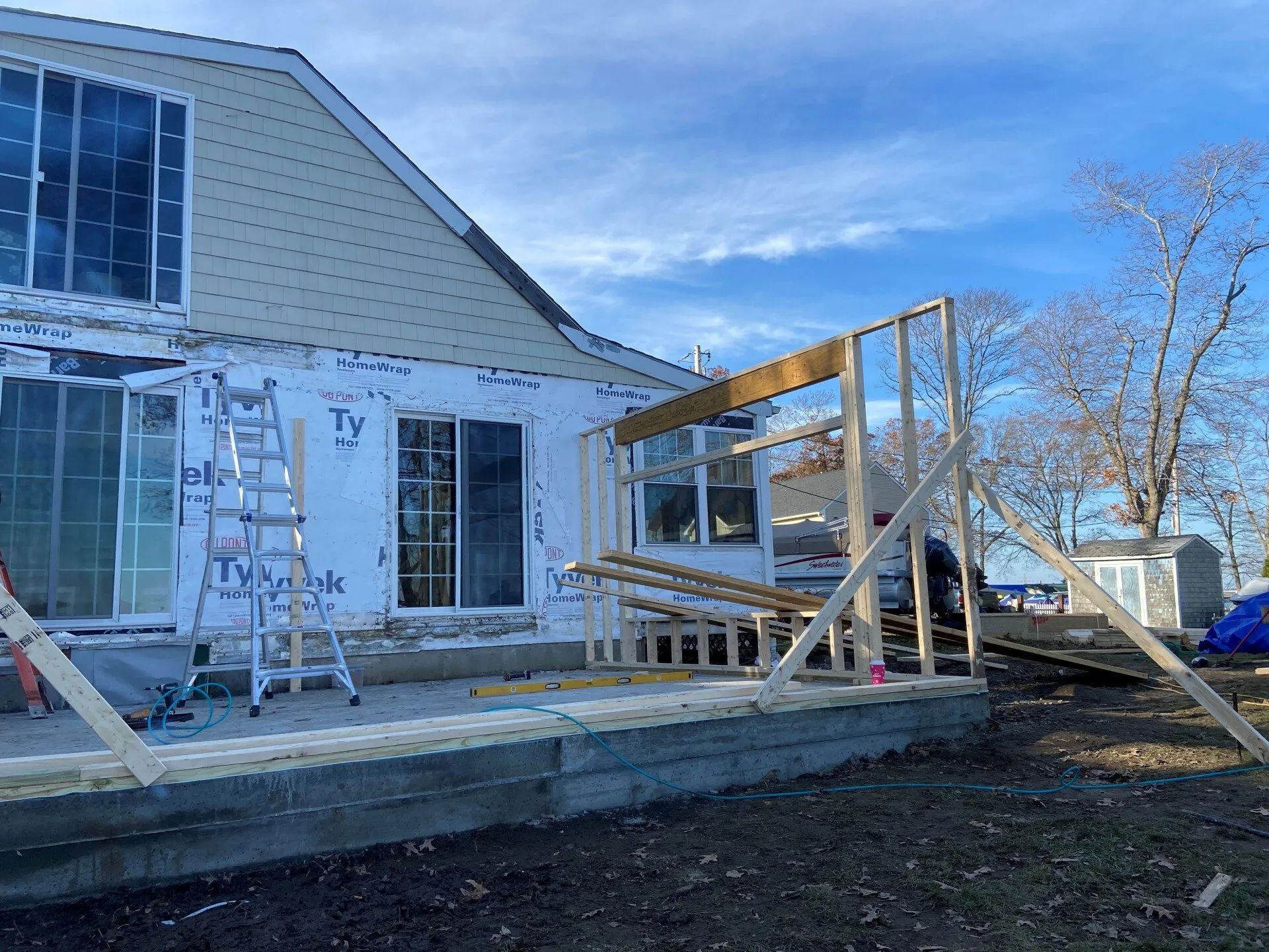 House exterior under construction with scaffolding, ladders, and wooden framing on a porch deck