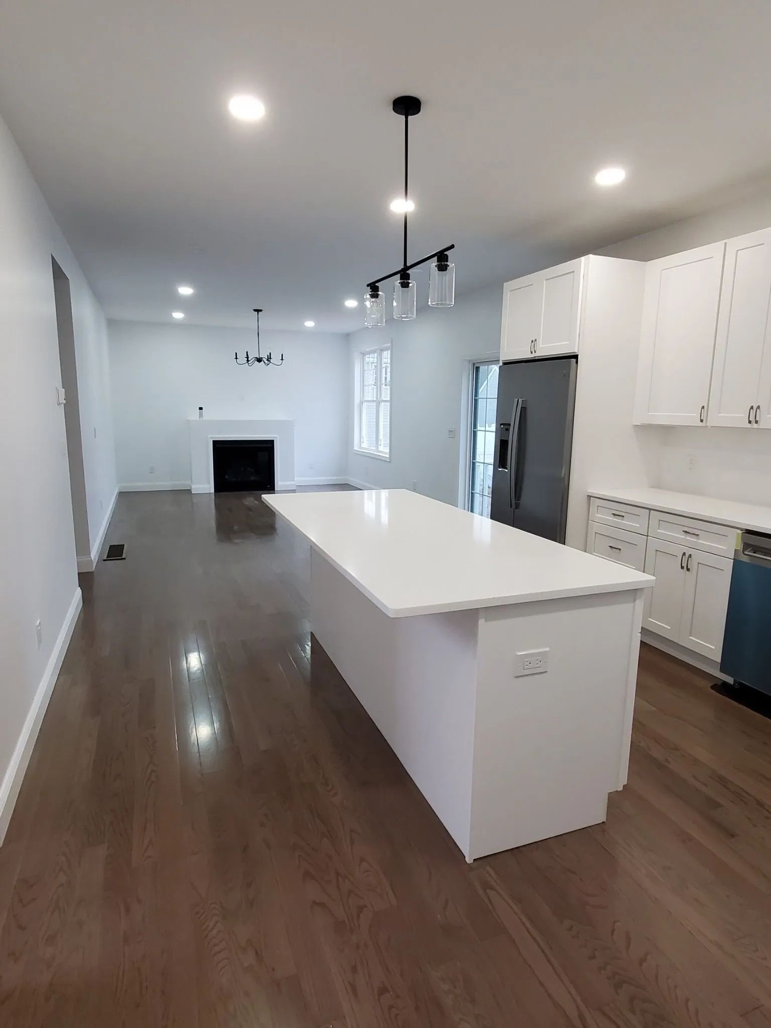 Bright modern kitchen with white cabinets, island, stainless fridge, and dark wood floors