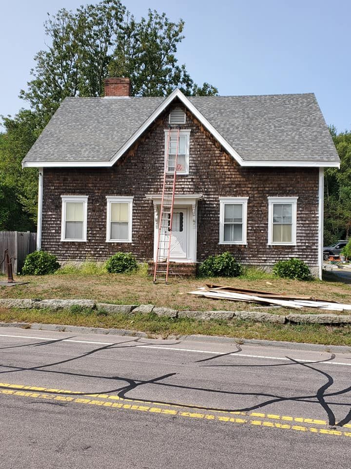 Small brown house with white trim and boarded windows beside a cracked street.