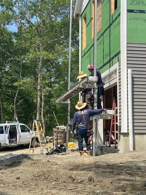 Two construction workers on scaffolding beside a green building under construction