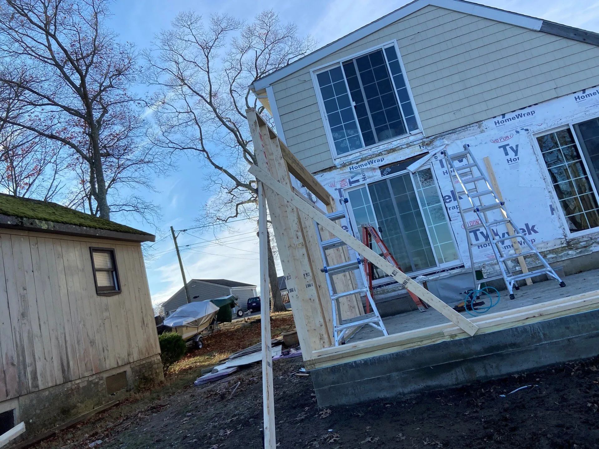 Damaged house exterior with leaning porch, cracked siding, and temporary support beams