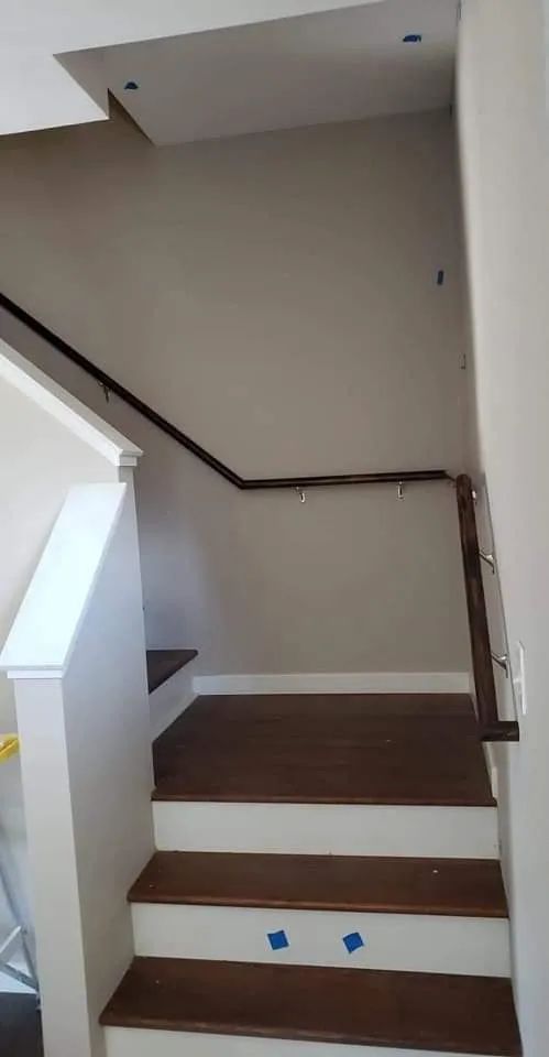 Indoor staircase with brown steps, white trim, and a beige wall beneath a sloped ceiling