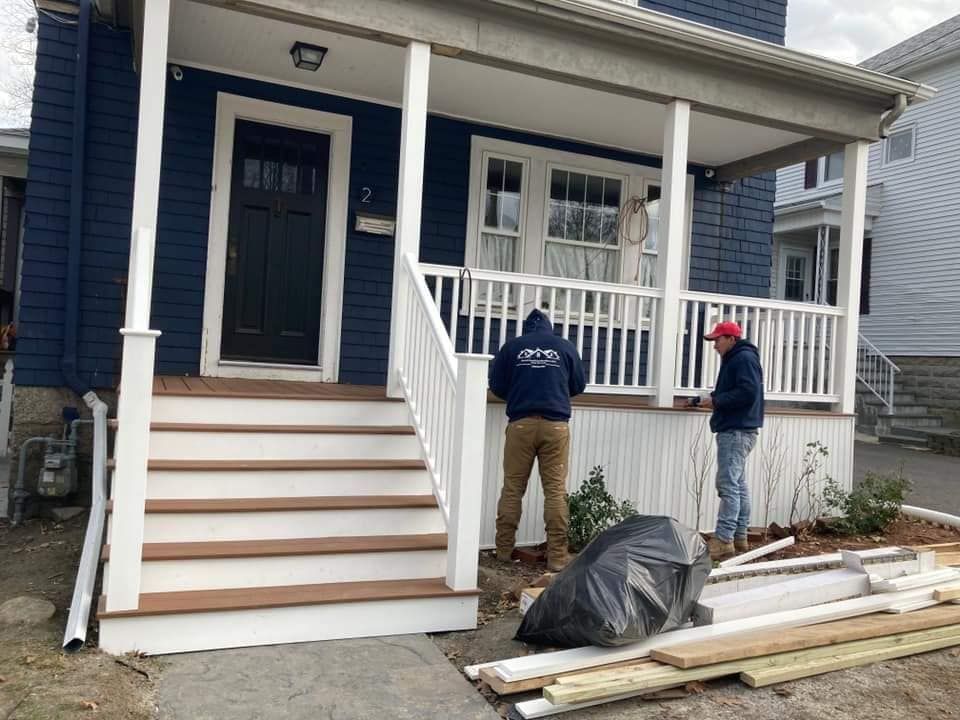 Two workers installing a front porch railing on a blue house with white trim