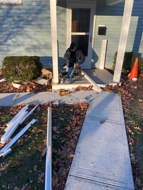 Person working at a front entrance with scattered white debris, a ramp, and an orange cone nearby.