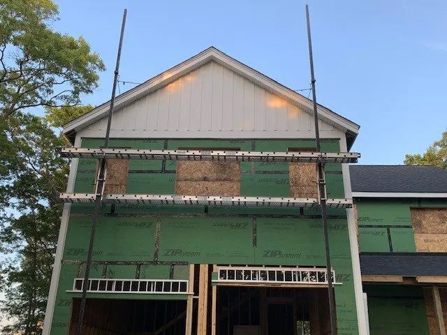 Green house under renovation with scaffolding, unfinished siding, and exposed brick facade