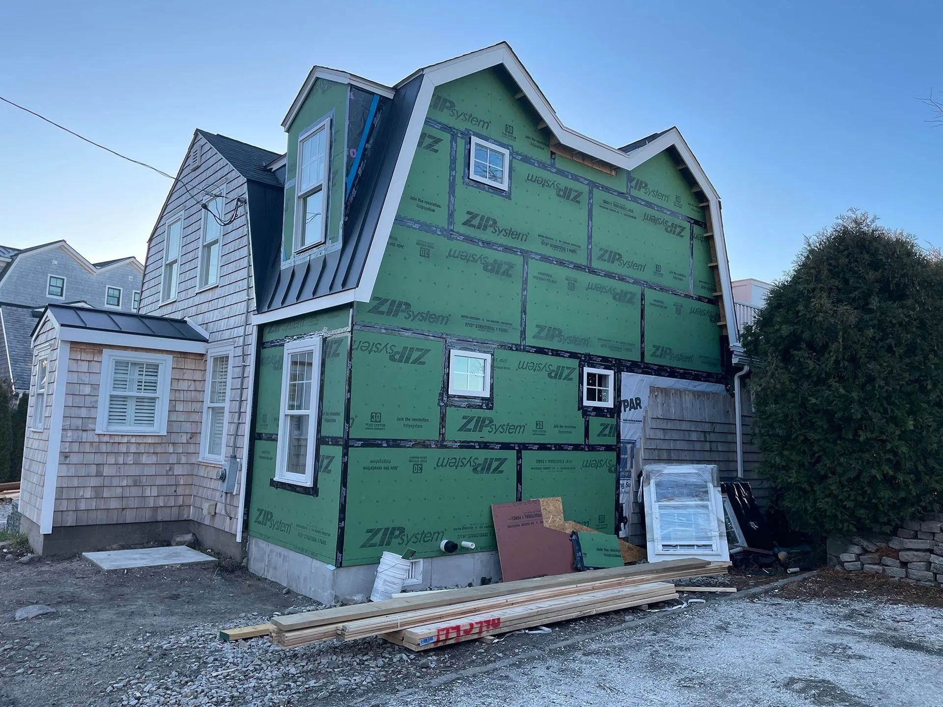Partially built house wrapped in green house wrap, with unfinished siding and construction materials outside.