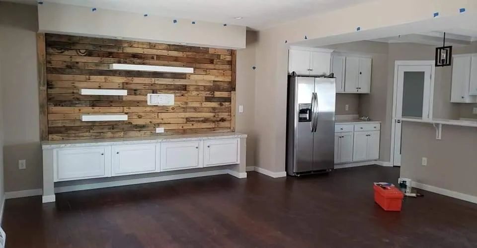 Empty modern kitchen-living space with white cabinets, wood accent wall, stainless fridge, and dark hardwood floors